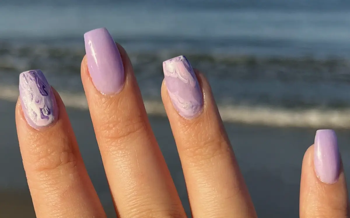 Lilac almond nails with marbled accents, held up against the ocean
