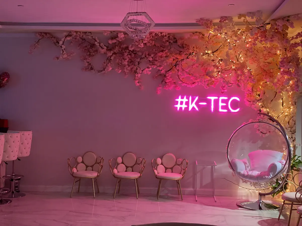 The salon's lounge: a pink neon #K-TEC sign under cherry blossom and fairy lights, gold petal chairs and a clear bubble chair